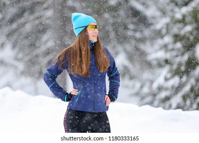 Young runner woman standing at the road in winter. Smiling girl resting after morning jog training enjoying winter weather