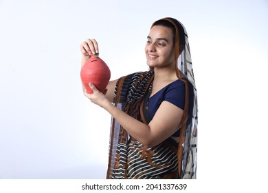 Young Rural Indian Bald Widow Saving Money Inserting A Coin In Piggy Bank, Wearing A Saree Portraying Various Expressions Of The Widow Life. She Is Confident And Portraying Savings Concept.