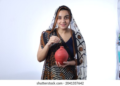 Young Rural Indian Bald Widow Saving Money Inserting A Coin In Piggy Bank, Wearing A Saree Portraying Various Expressions Of The Widow Life. She Is Confident And Portraying Savings Concept.