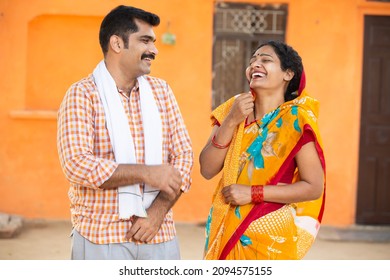 Young rural indian couple standing laughing outdoor at village house. Mustache man wearing kurta and woman wearing sari, husband wife wearing traditional cloths having fun candid moment. - Shutterstock ID 2094575155