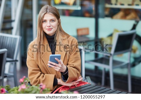 A young Russian girl is typing a message on the phone. Moscow. Autumn. A girl writes SMS message. Communicates in social networks. Woman sitting in a cafe in the city center.