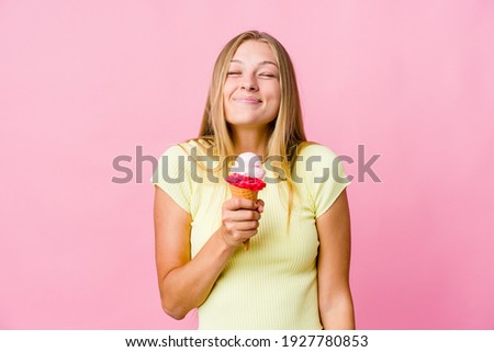 Young russian woman eating an ice cream isolated laughs and closes eyes, feels relaxed and happy.