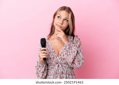 Young Russian woman holding a microphone isolated on pink background having doubts - Powered by Shutterstock