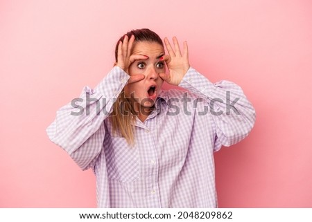 Young Russian woman isolated on pink background points sideways, is trying to choose between two options.