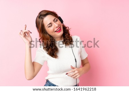 Young Russian woman over isolated pink background using the mobile with headphones and dancing