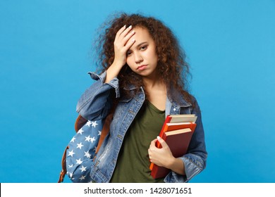 Young Sad African American Girl Teen Student In Denim Clothes, Backpack Hold Books Isolated On Blue Background Studio Portrait. Education In High School University College Concept. Mock Up Copy Space