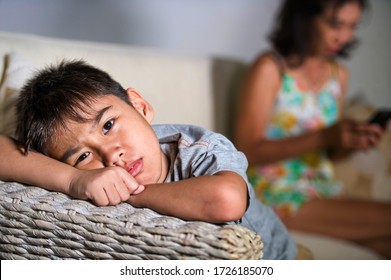 Young Sad And Bored 7 Asian Child At Home Couch Feeling Frustrated And Neglected While Mother Using Mobile Phone As Internet Addict Neglecting Her Son During Covid-19 Stay Home Lockdown