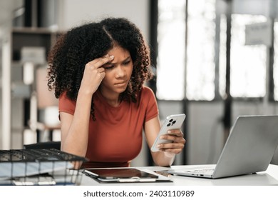 Young sad businesswoman is sitting at table, covering his face with his hand and talking on cell phone. On desk is laptop, tablet computer, Stress. - Powered by Shutterstock