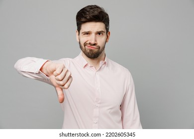 Young Sad Caucasian Disappointed Upset Disappointed Man 20s He Wearing Basic White Shirt Showing Thumb Down Dislike Gesture Isolated On Plain Grey Background Studio Portrait. People Lifestyle Concept