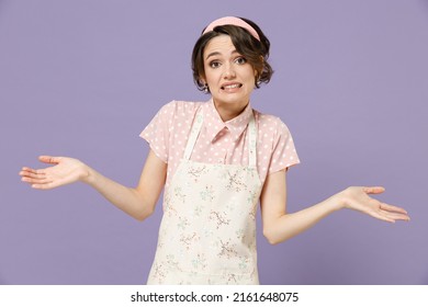 Young Sad Clueless Uncertain Doubtful Confused Sad Housewife Housekeeper Chef Cook Baker Woman In Pink Apron Spreading Hands Isolated On Pastel Violet Background Studio Portrait. Cooking Food Concept.