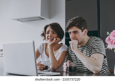 Young Sad Confused Couple Two Woman Man In Casual T-shirt Clothes Sit Table Drink Coffee Using Laptop Pc Computer Ith Virus Do Oops Gesture In Light Kitchen At Home Together People Lifestyle Concept