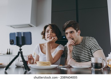 Young Sad Confused Disappointed Couple Two Woman Man In Casual Clothes Sit By Table Eat Pancake Watch Live Stream By Mobile Cell Phone Cook Food In Light Kitchen At Home Together Healthy Diet Concept