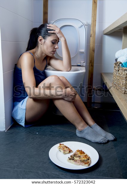 young\
sad and depressed bulimic woman feeling sick guilty after vomiting\
and throwing up kneeling on floor of toilet WC guilty eating pizza\
in nutrition disorder bulimia and anorexia\
concept