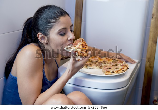 栄養障害の過食症の考え方でピザを食べるwcに寄り掛かるトイレの床に座り込んで 気分が悪く 憂鬱な若い女性 の写真素材 今すぐ編集
