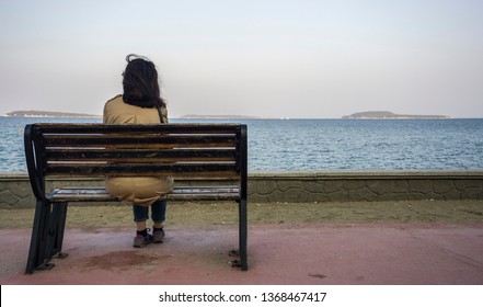 Young Sad Depressed Woman Sit Alone On Bench, Looking At Distant Sea / Seascape Horizon. Time To Go, Say Goodbye. Miss Someone. Desire, Hope To Go Far Away. Unhappy Girl Feel Lonely At Seaside Outdoor