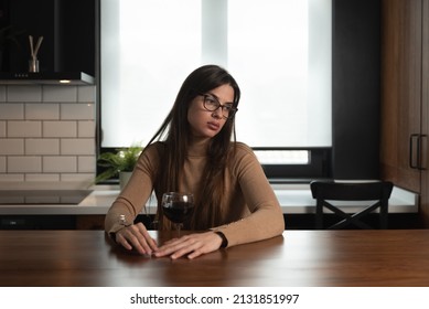 Young Sad Depressed Woman Sitting Alone At Home Drinking Wine Feeling Abandoned. Anxious Female Suffering From Depression After Relationship Breakup Drinking Alcohol Drink In Kitchen Try Not To Cry.