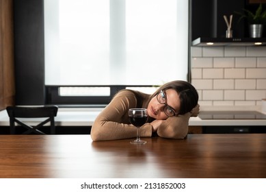 Young Sad Depressed Woman Sitting Alone At Home Drinking Wine Feeling Abandoned. Anxious Female Suffering From Depression After Relationship Breakup Drinking Alcohol Drink In Kitchen Try Not To Cry.