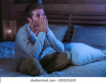 young sad and desperate man awake late night on bed in darkness suffering depression and anxiety looking stressed crying alone holding pillow at harsh dramatic lightened bedroom 