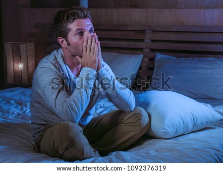 young sad and desperate man awake late night on bed in darkness suffering depression and anxiety looking stressed crying alone holding pillow at harsh dramatic lightened bedroom 
