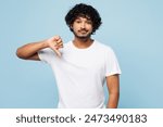 Young sad disappointed upset Indian man he wear white t-shirt casual clothes showing thumb down dislike gesture isolated on plain pastel light blue cyan background studio portrait. Lifestyle concept