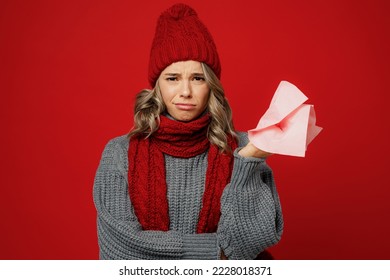 Young sad displeased upset woman wear grey sweater scarf hat hold in hand pink napkin isolated on plain red background studio portrait Healthy lifestyle ill sick disease treatment cold season concept - Shutterstock ID 2228018371