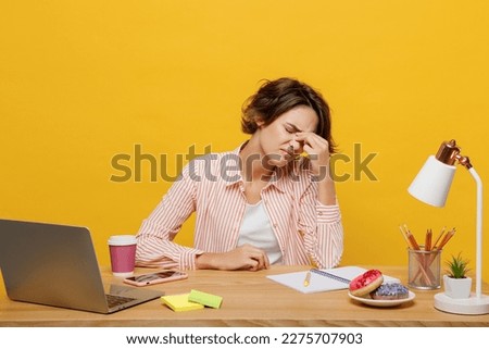 Young sad employee business woman wear casual shirt sit work at office desk with pc laptop keep eyes closed rub put hand on nose isolated on plain yellow color background. Achievement career concept