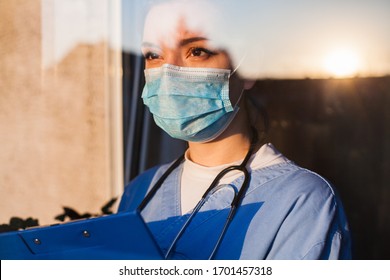 Молодая грустная женщина кавказская британская врач скорой помощи США смотрит через окно реанимации, боится неуверенности в глазах, носит маску для лица, смотрит на солнце, надеется на веру в преодоление кризиса пандемии коронавируса COVID-19 