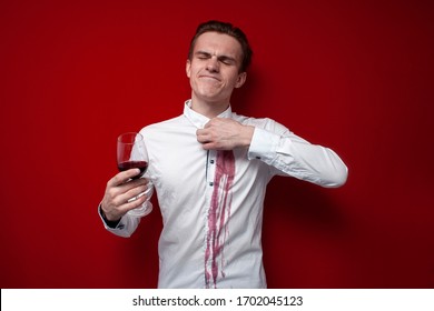 young sad guy in a white shirt spilled red wine on himself on a red background, an angry man put a stain of wine on his clothes