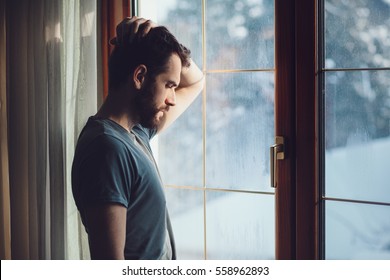 Jovem triste louco sentado perto da janela em arrependimento
