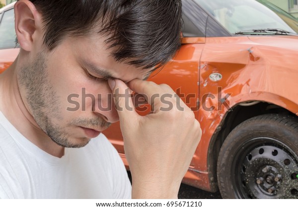 Young sad man had car accident. Damaged car
in background.