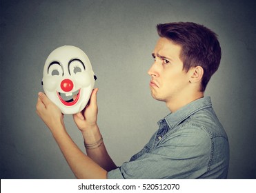 Young Sad Man With Happy Clown Mask Isolated On Gray Wall Background. Human Emotions. Split Personality Concept  