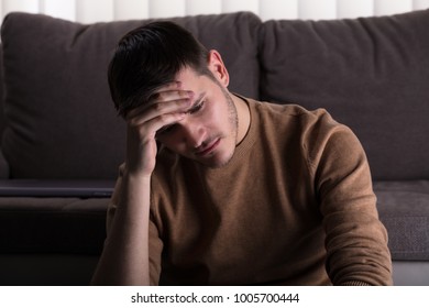 Young Sad Man Sitting In Front Of Sofa At Home