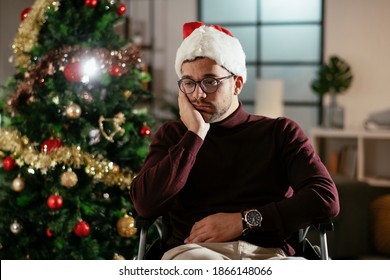 Young Sad Man In Wheelchair Sitting Near Christmas Tree. 