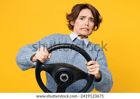 Young sad scared astonished woman she wears grey knitted sweater shirt casual clothes hold steering wheel driving car look camera isolated on plain yellow background studio portrait. Lifestyle concept