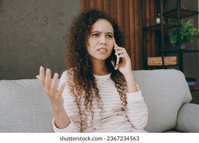 Young sad upset woman wearing casual clothes sits on grey sofa couch talking speak on mobile cell phone stay at home hotel flat rest relax spend free spare time in living room indoor. Lounge concept - Shutterstock ID 2367234563
