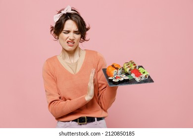 Young Sad Woman 20s In Casual Clothes Hold In Hand Makizushi Sushi Roll Served On Black Plate Traditional Japanese Food Showing Stop Gesture With Palm Refuse Isolated On Plain Pastel Pink Background.