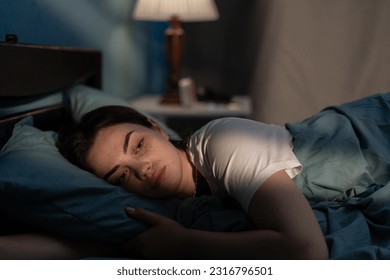 Young sad woman lying in bed late at night trying to sleep suffering insomnia. Girl in bed scared on nightmares looking worried and stressed. Sleeping disorder and insomnia concept - Powered by Shutterstock