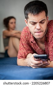 A Young Sad Woman Is Next To Her Partner Who Is Texting On The Phone With Someone, And Not Paying Attention To Her.