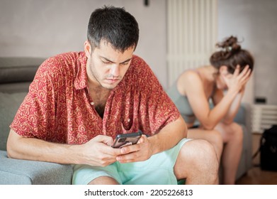 A Young Sad Woman Is Next To Her Partner Who Is Texting On The Phone With Someone, And Not Paying Attention To Her.