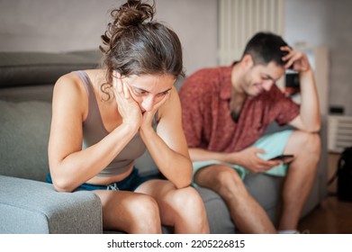 A Young Sad Woman Is Next To Her Partner Who Is Texting On The Phone With Someone, And Not Paying Attention To Her.