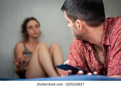 A Young Sad Woman Is Next To Her Partner Who Is Texting On The Phone With Someone, And Not Paying Attention To Her.