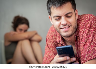 A Young Sad Woman Is Next To Her Partner Who Is Texting On The Phone With Someone, And Not Paying Attention To Her.