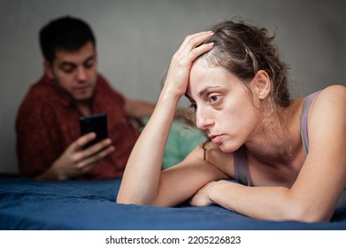 A Young Sad Woman Is Next To Her Partner Who Is Texting On The Phone With Someone, And Not Paying Attention To Her.