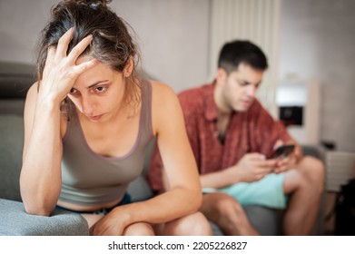 A Young Sad Woman Is Next To Her Partner Who Is Texting On The Phone With Someone, And Not Paying Attention To Her.