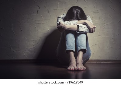 Young sad woman sitting alone on the floor in an empty room