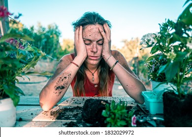 Young Sad Woman Wearing A Red Dress Surrounded By Plants And Pots On A Wooden Table