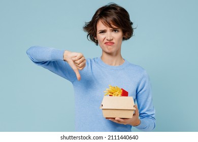 Young Sad Woman Wearing Sweater Hold A Box With Fastfood French Fries Potato Burger Show Thumb Down Dislike Gesture Isolated On Plain Pastel Light Blue Background. People Lifestyle Junk Food Concept