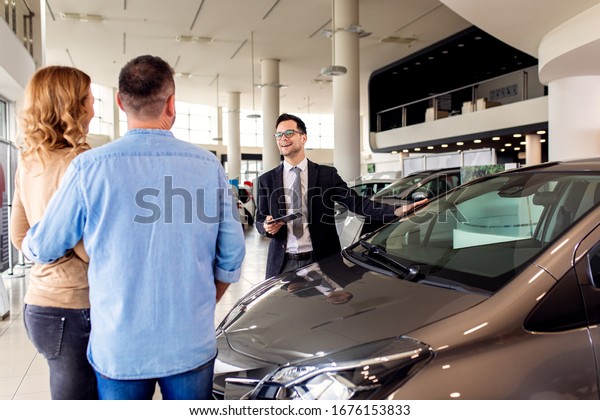 Young sales agent helping adult couple to\
choose a new car in modern car\
showroom.