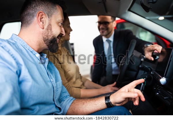 Young sales agent helping adult couple to
choose a new car in modern car
showroom.
