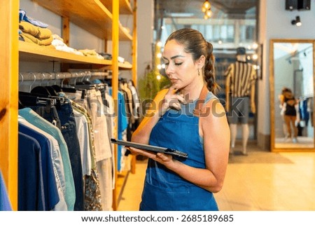 Young sales assistant using a digital tablet and checking clothes inventory in a fashion store